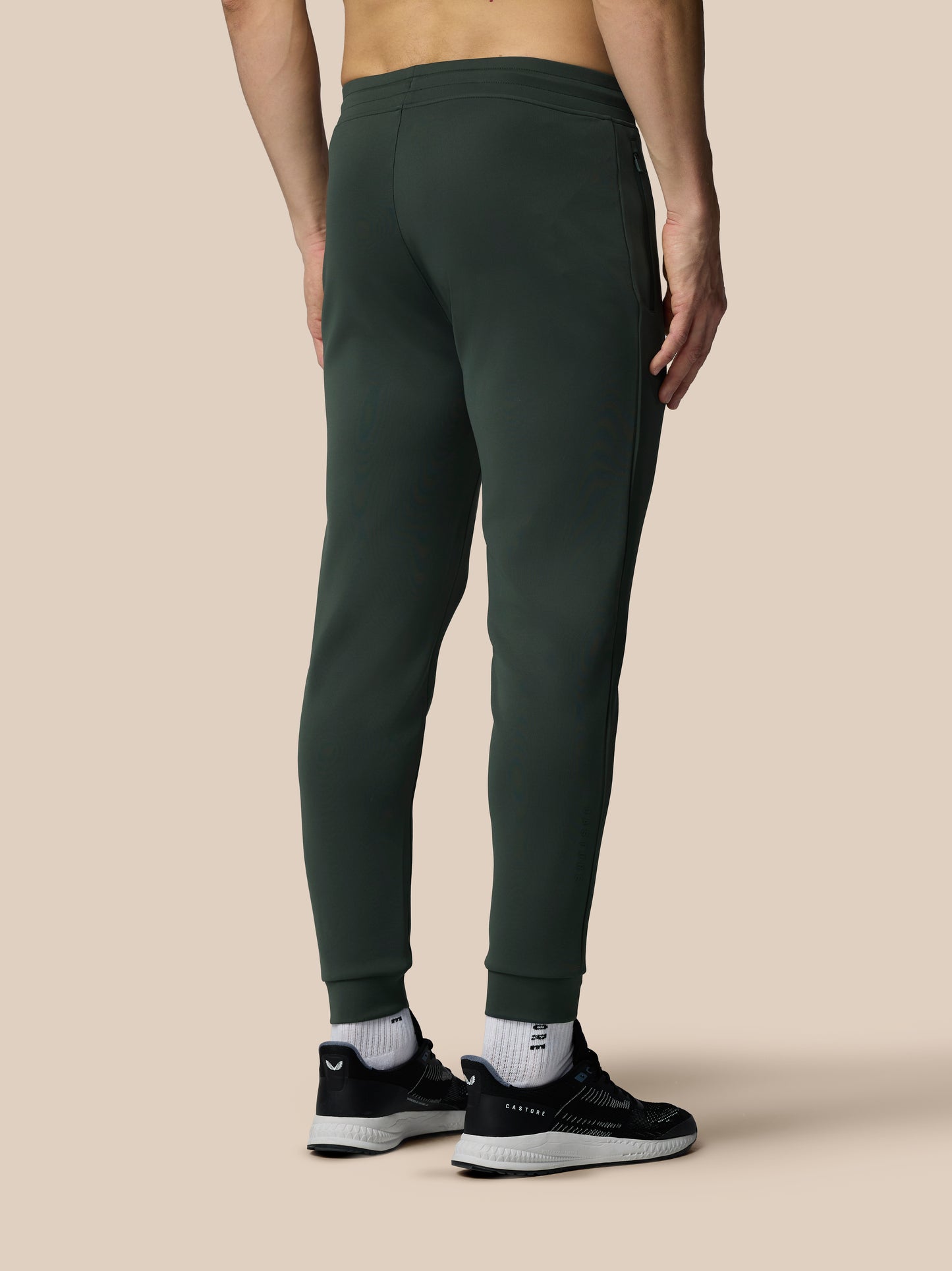Person wearing dark green sweatpants on a beige background