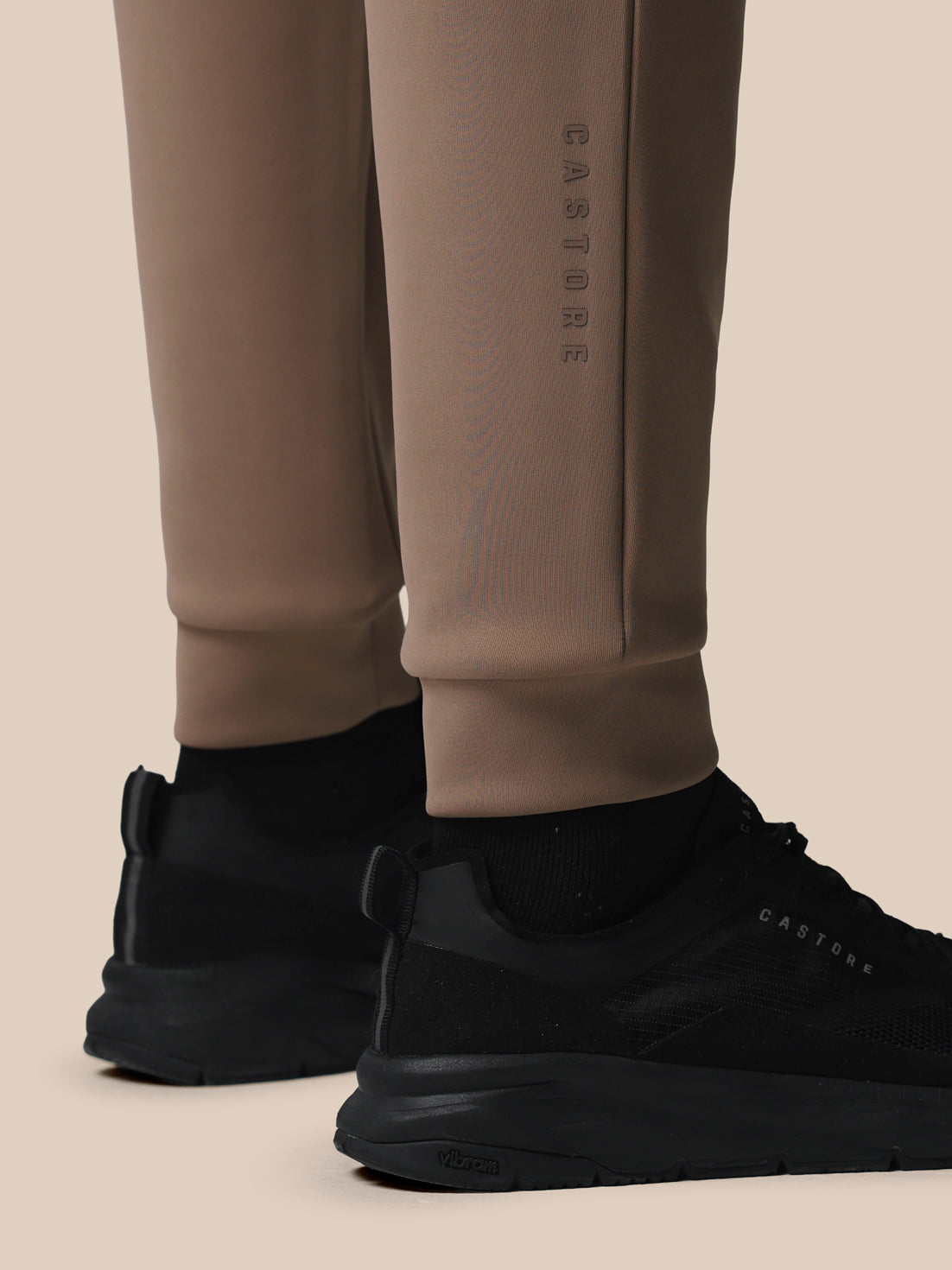Beige pants with a brand logo and black shoes on a beige background