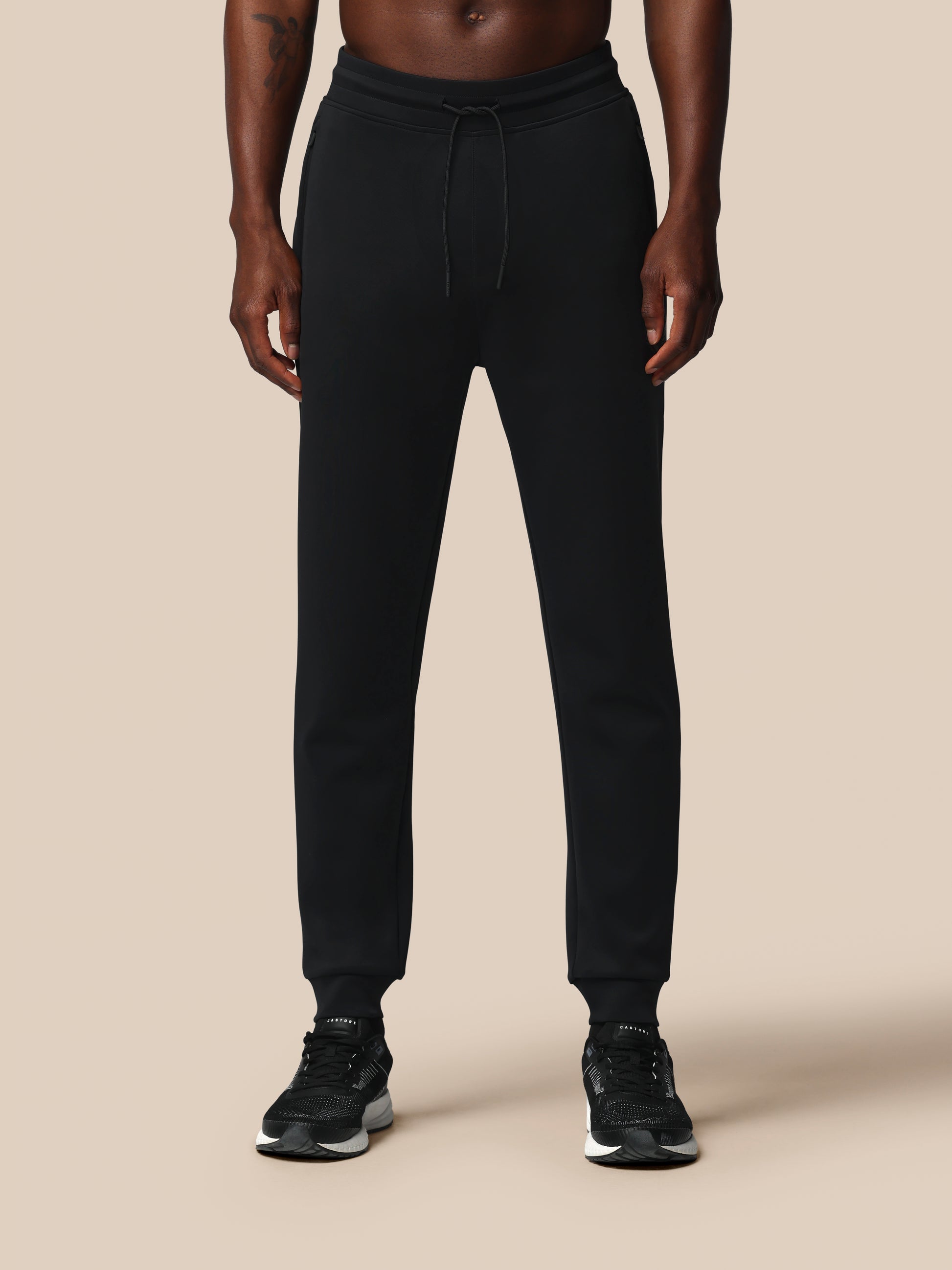 Person wearing black jogger pants on a beige background