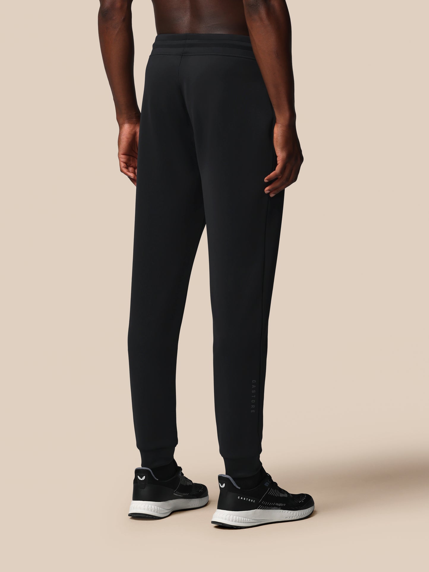 Person wearing black athletic pants and shoes on a beige background