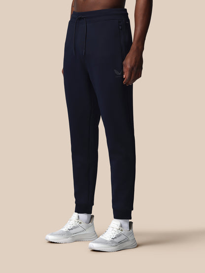 Person wearing navy jogger pants and white sneakers on a beige background