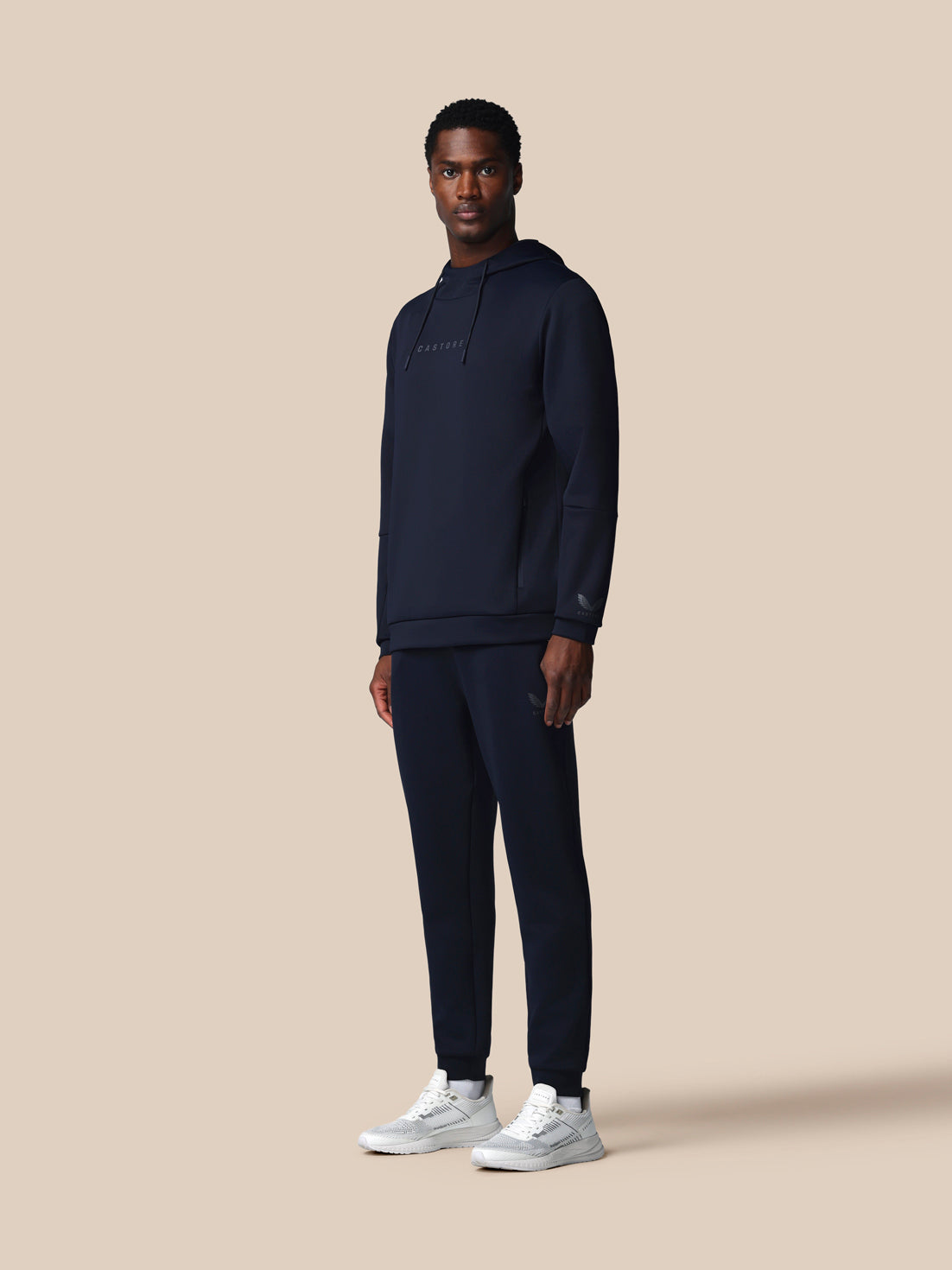 Man wearing a navy tracksuit with 'CASTORE' branding on a beige background