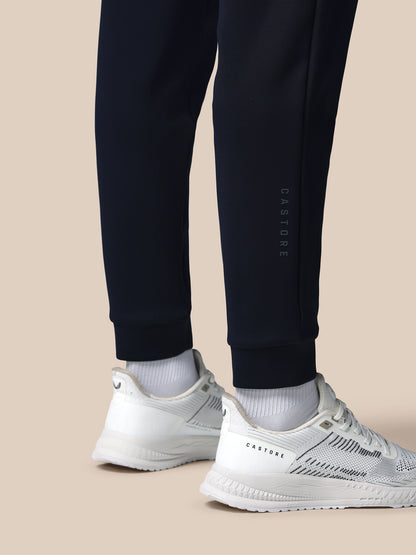 Person wearing black jogger pants and white sneakers on a beige background