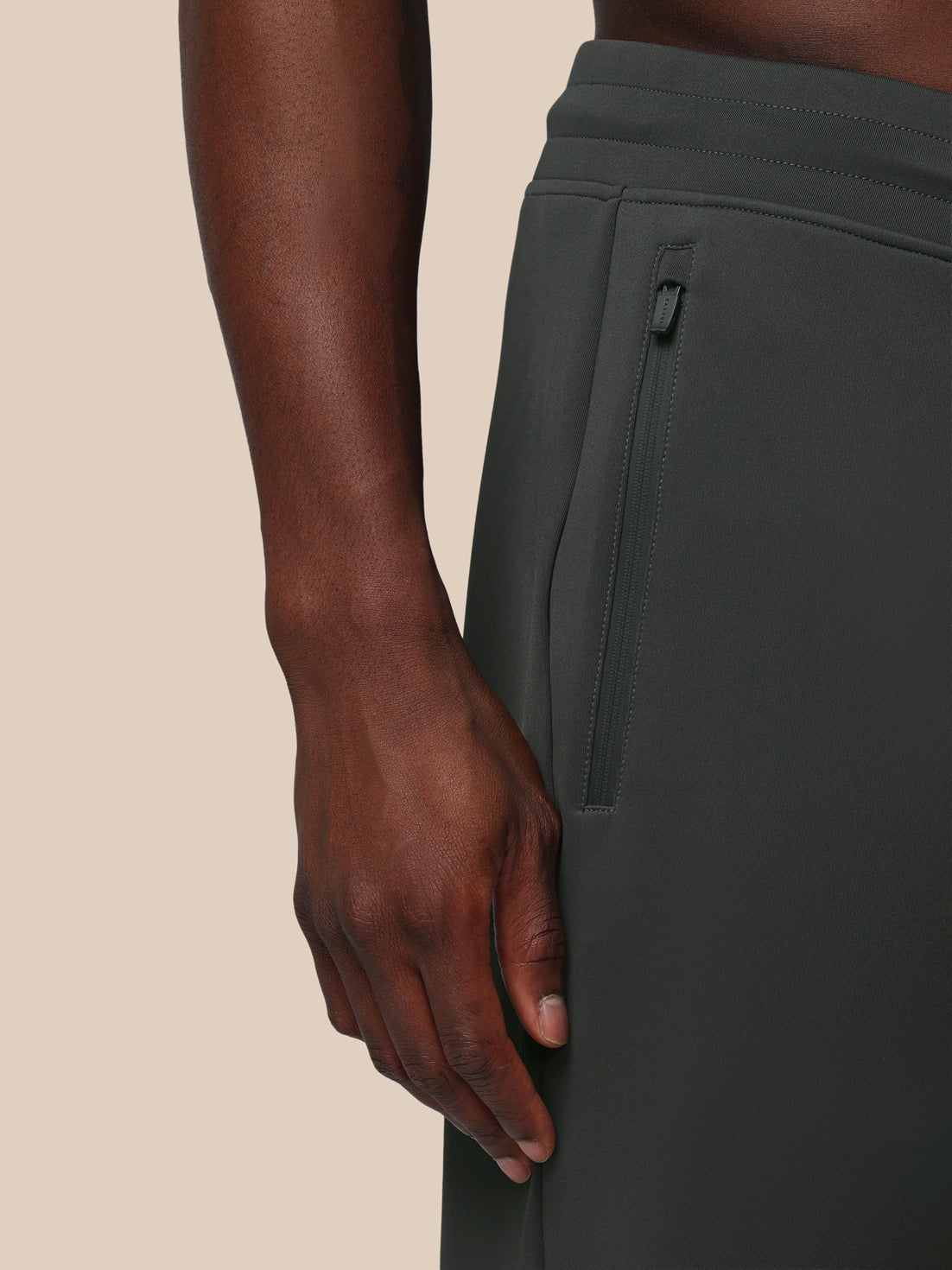Person wearing dark green pants with a beige background