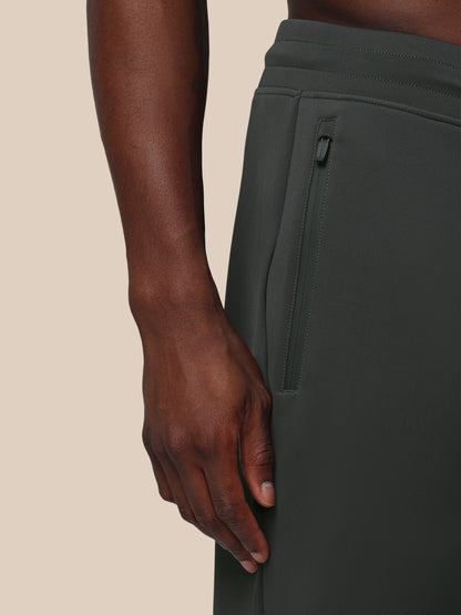 Person wearing dark green pants with a beige background