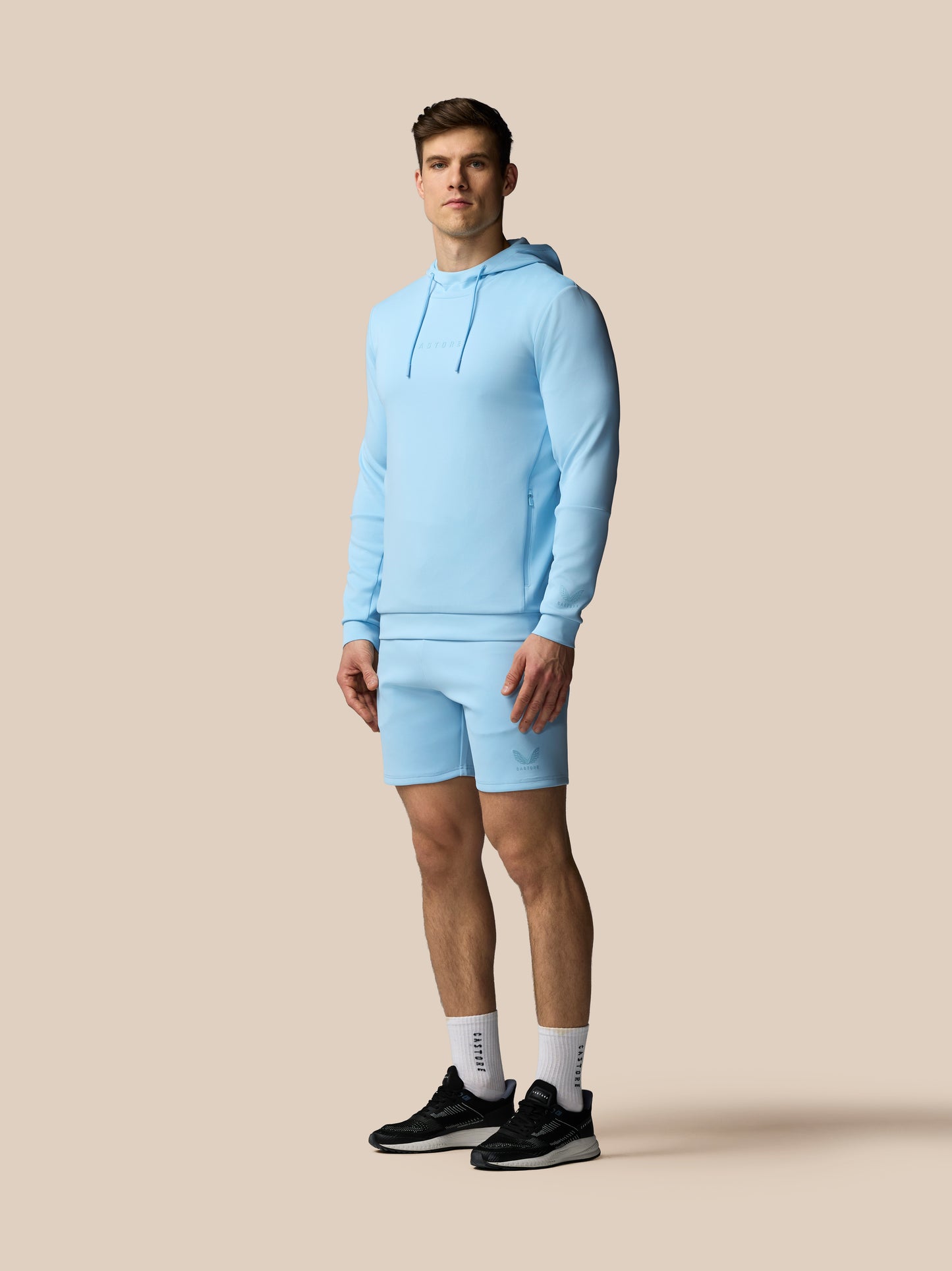 Man wearing a light blue hoodie and shorts on a beige background