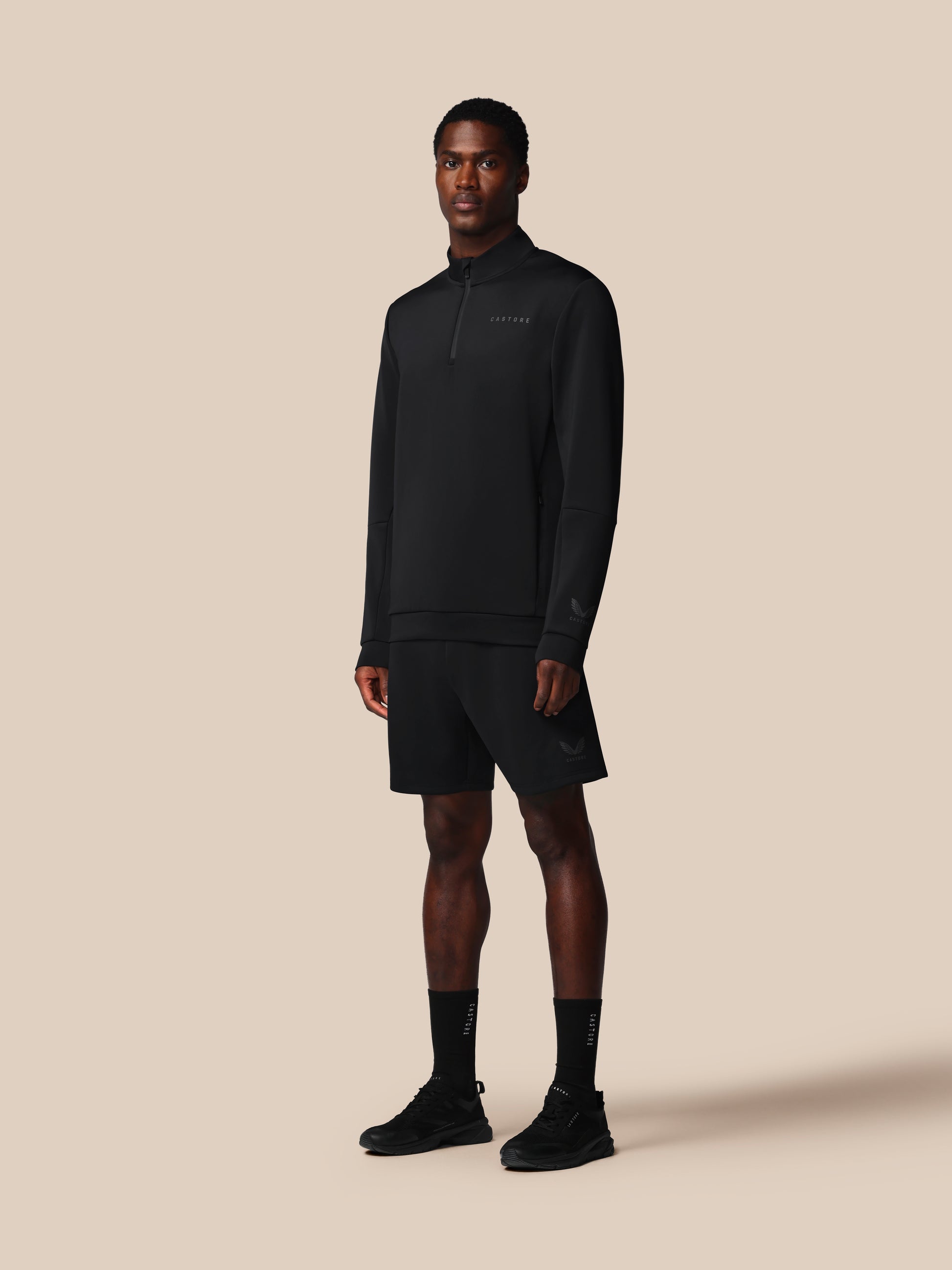 Man wearing a black pullover, shorts, and socks on a beige background