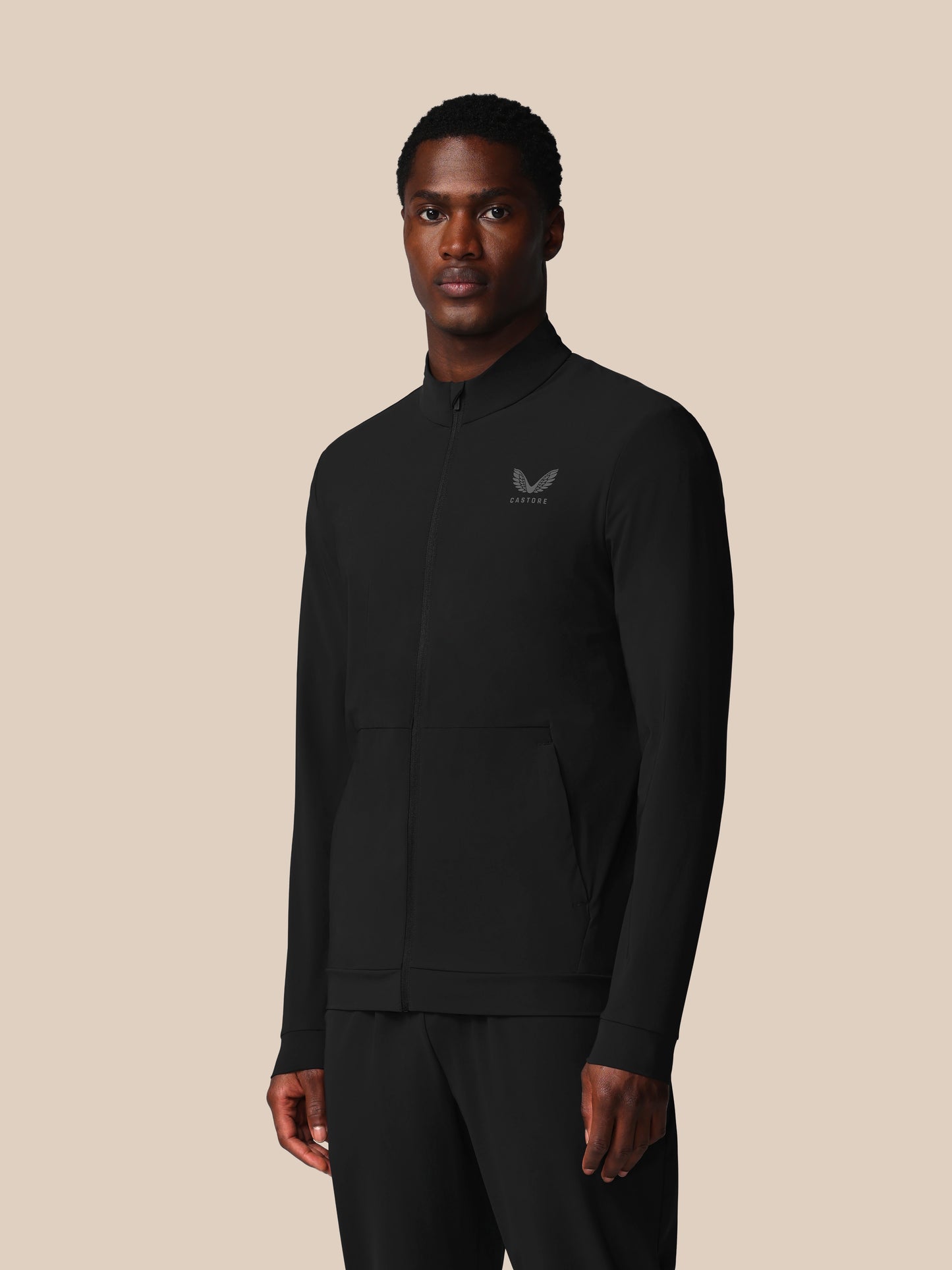 Man wearing a black jacket with a logo on a beige background