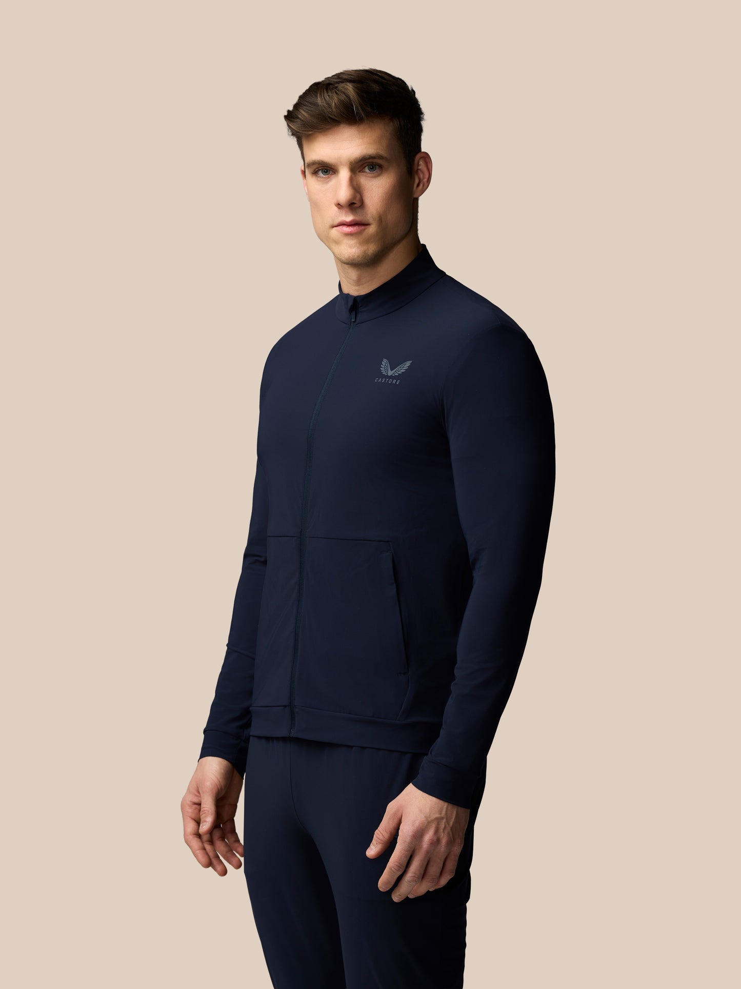 Man wearing a navy tracksuit with a logo on a beige background