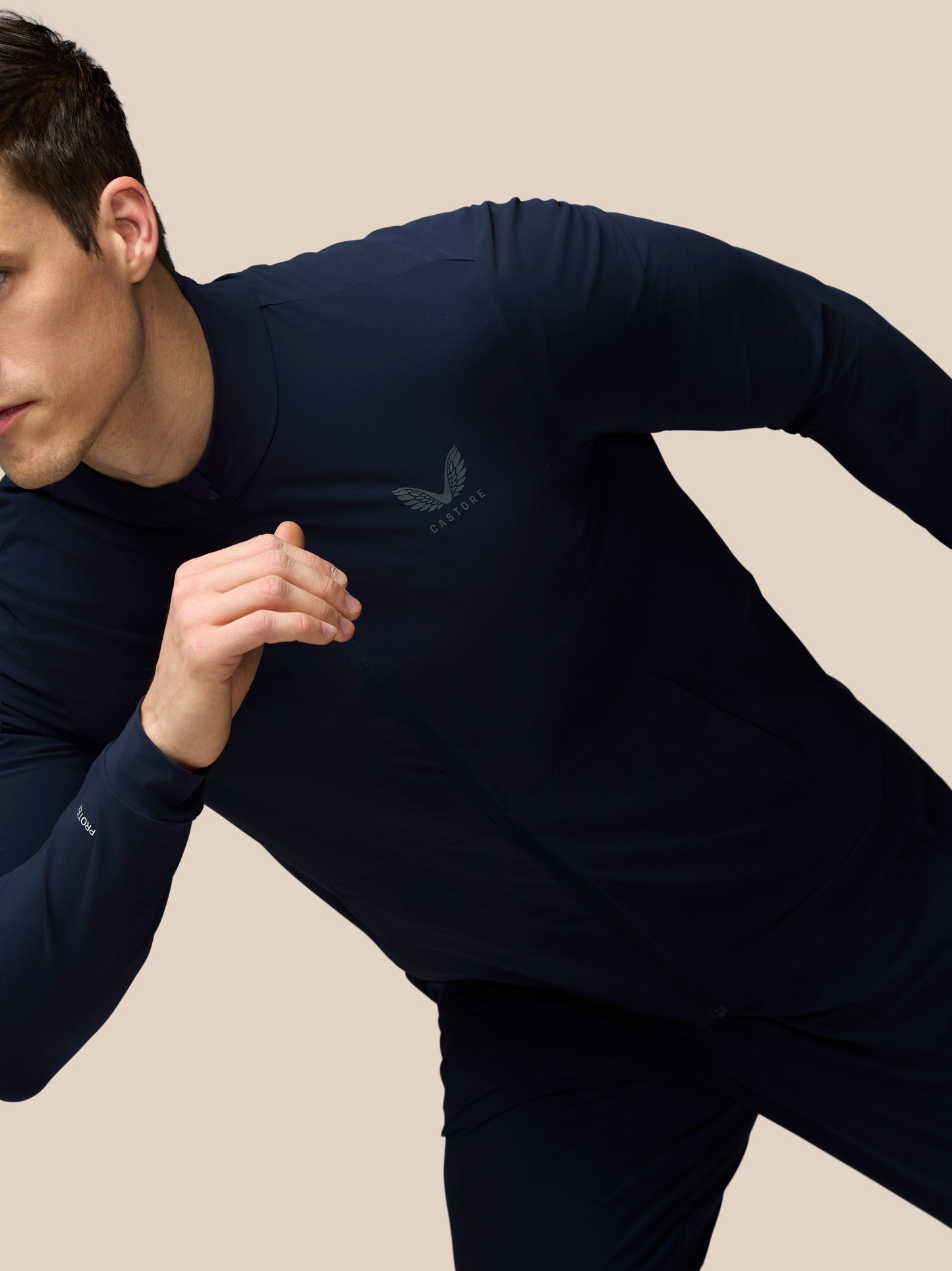 Man wearing a navy long-sleeve athletic shirt with a logo on a beige background