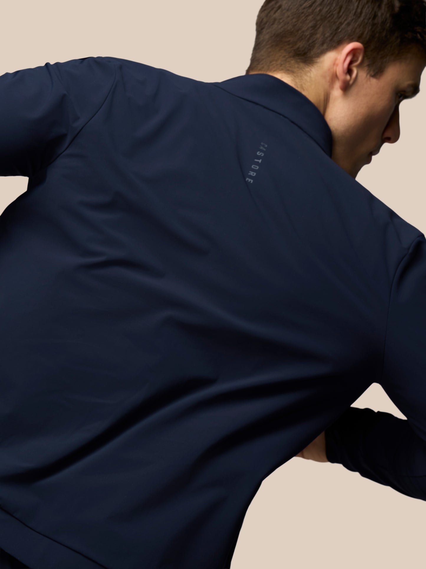Person wearing a navy blue shirt with a brand logo on a beige background