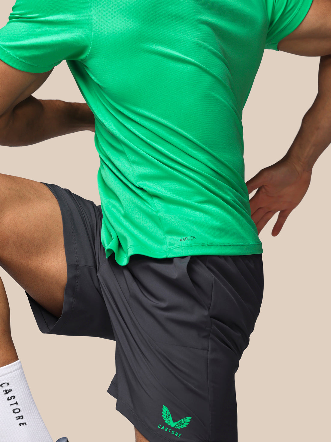 Person wearing a green athletic shirt and black shorts with a brand logo on a beige background
