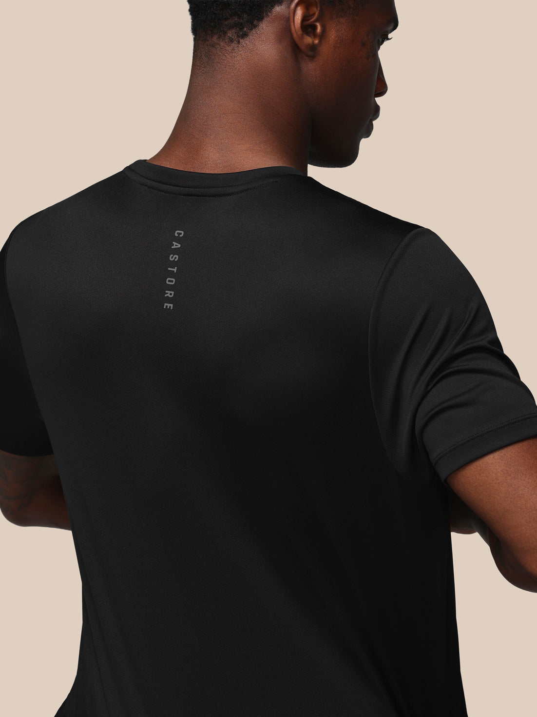 Person wearing a black t-shirt with a brand logo on the back against a beige background