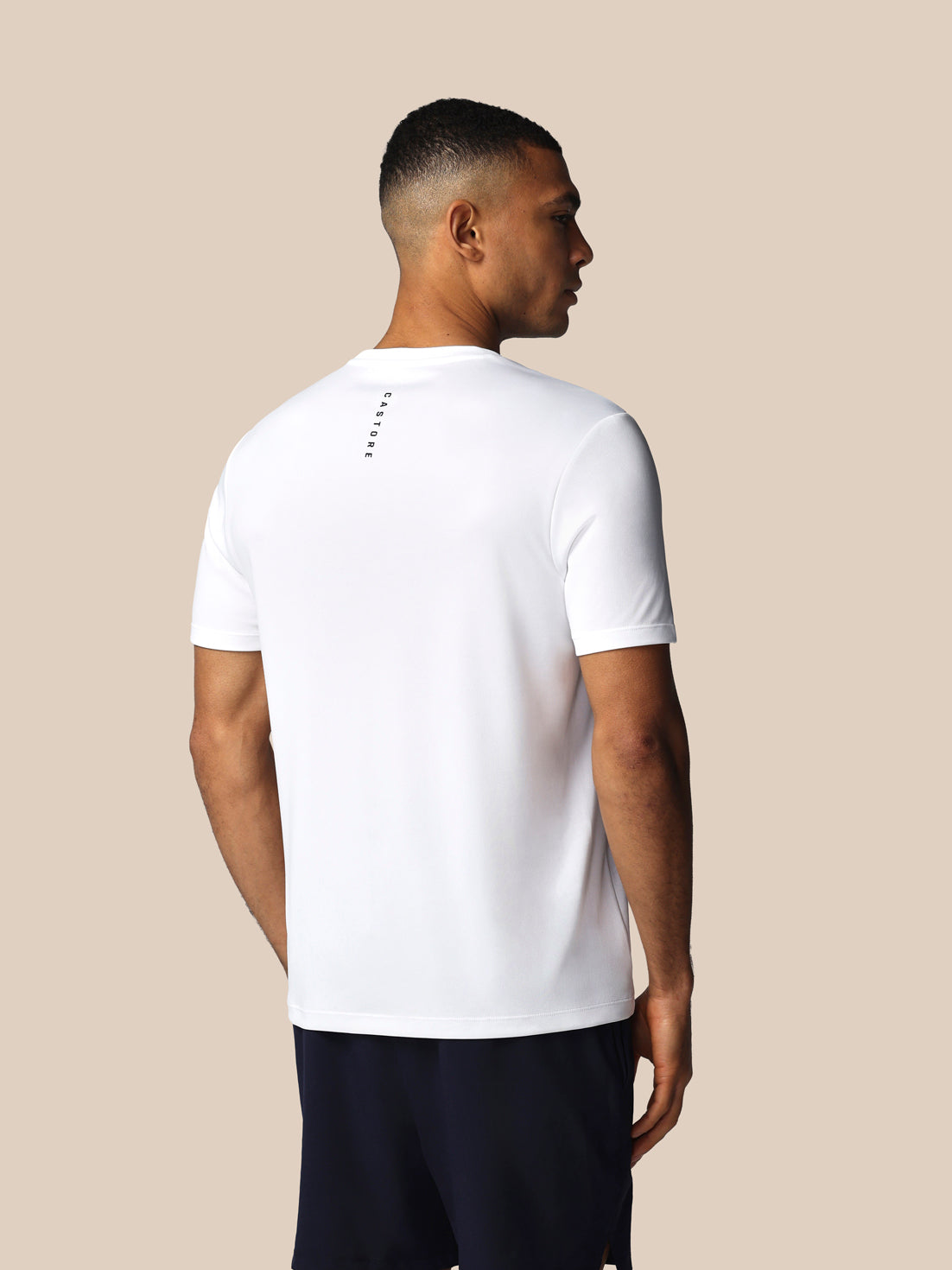 Man wearing a white t-shirt with a subtle design on the back against a beige background