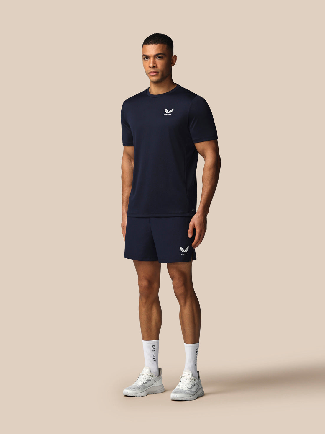Man wearing a navy athletic outfit with a logo on a beige background