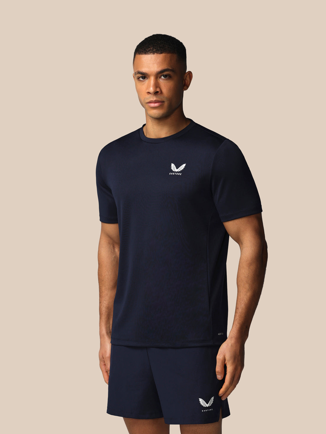 Man wearing a navy blue athletic outfit with a logo on a beige background