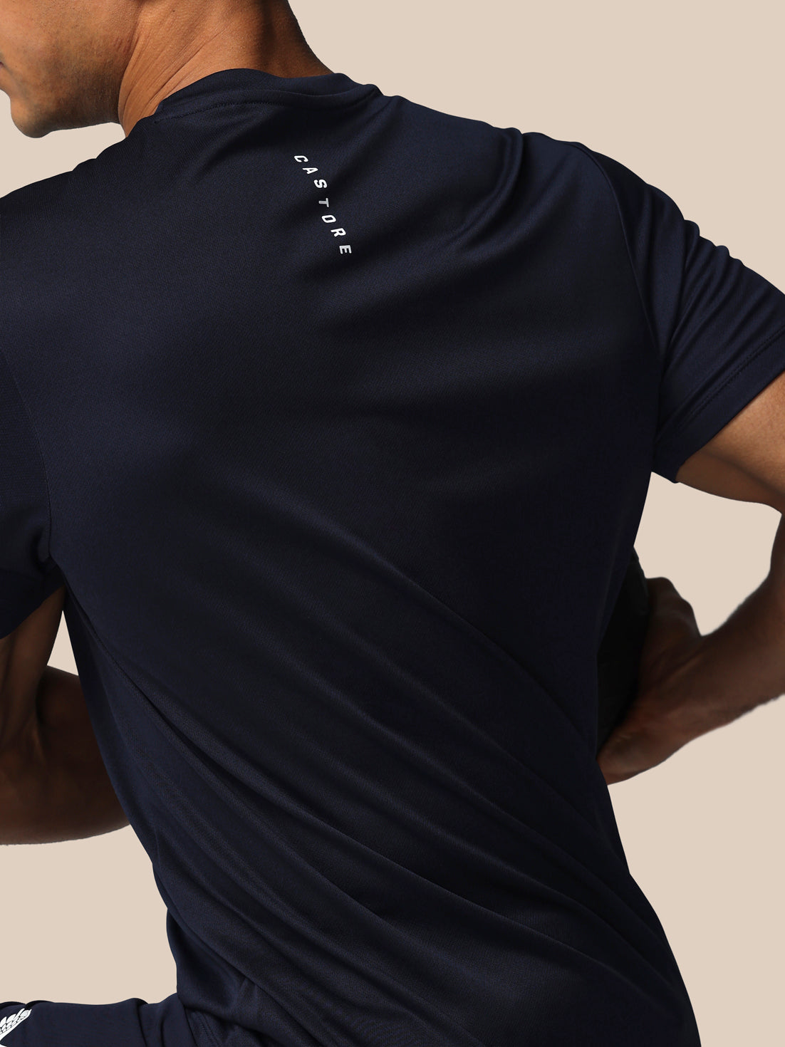 Person wearing a black athletic shirt with a brand logo on the shoulder against a beige background