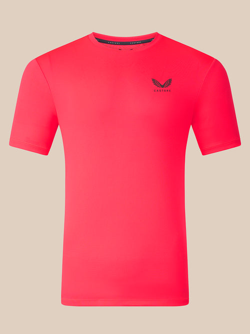 A bright pink short-sleeve athletic t-shirt with a small black winged logo and the brand name 'CASTORE' printed on the left chest, displayed on a solid beige background.