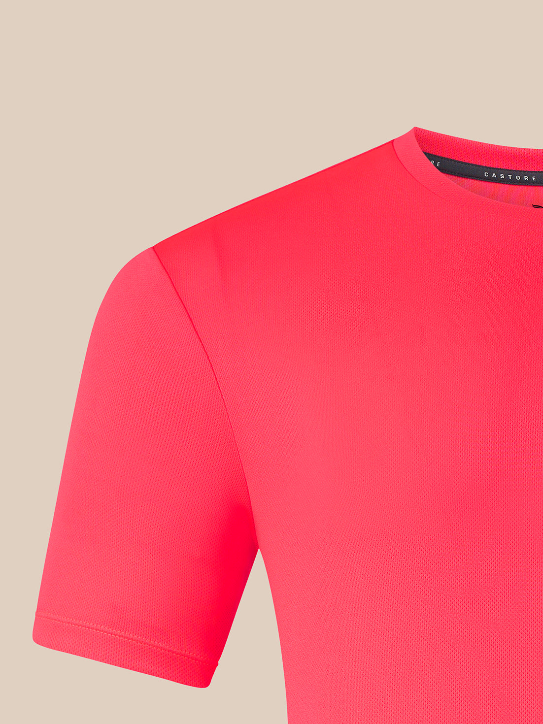 A close-up of a bright pink short-sleeve knit top, showing the shoulder, sleeve, and crew neckline against a solid beige background.