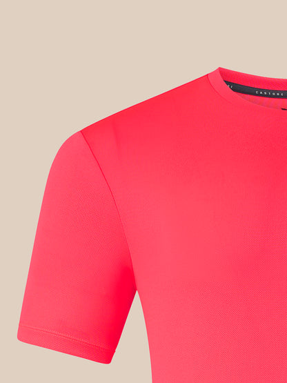A close-up of a bright pink short-sleeve knit top, showing the shoulder, sleeve, and crew neckline against a solid beige background.
