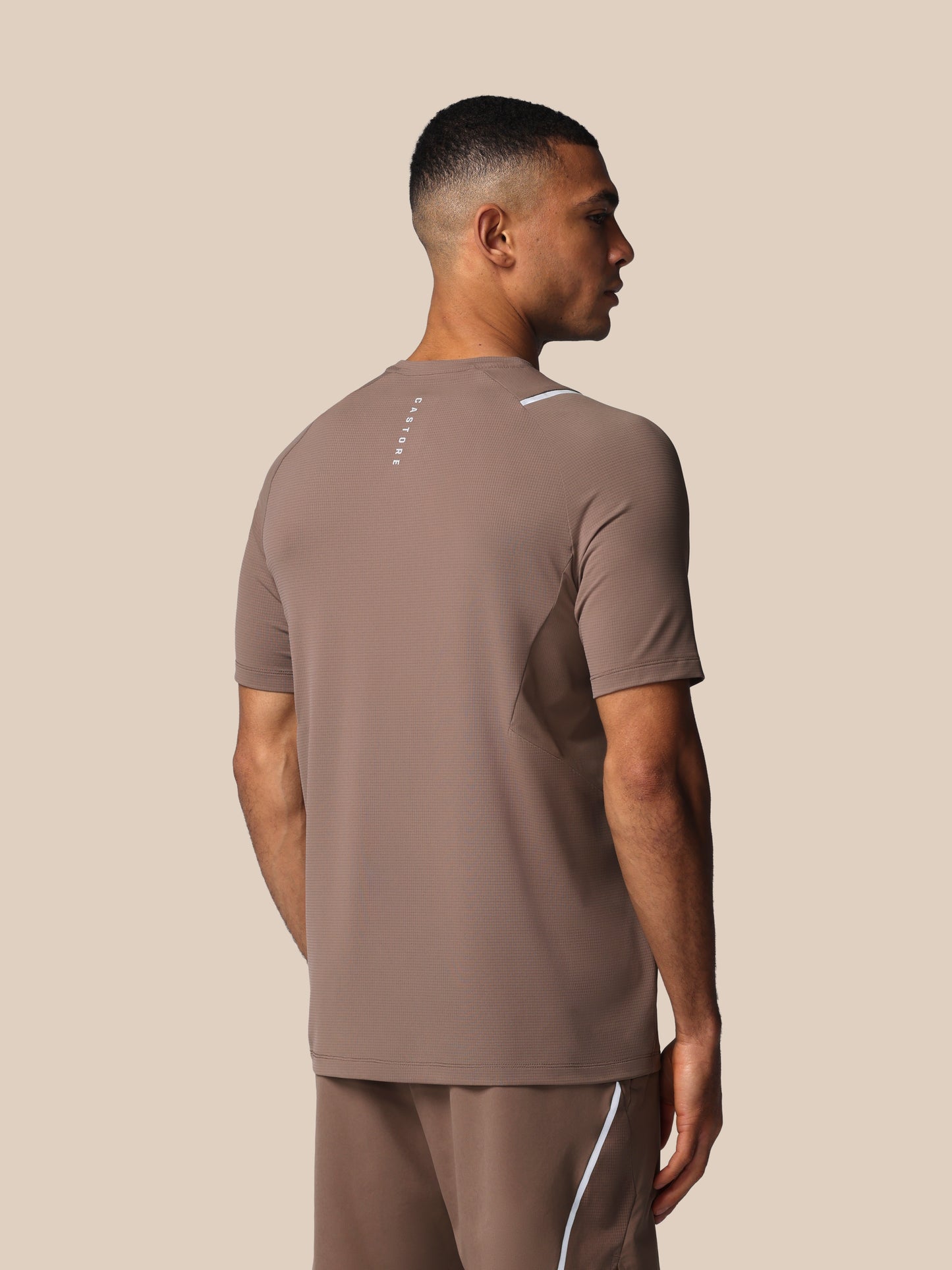 Man wearing a brown athletic outfit with a Castore logo on a beige background