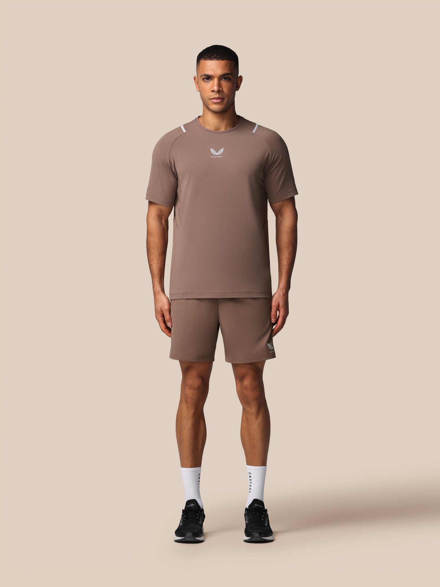 Man wearing a brown athletic outfit with a logo on a beige background
