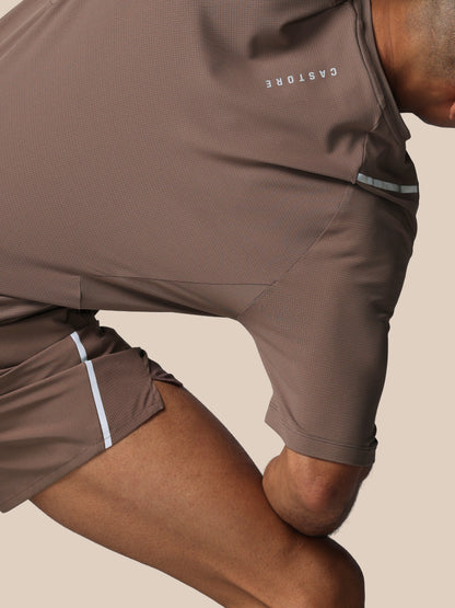 Person wearing brown athletic shorts with 'CASTORE' branding on a beige background