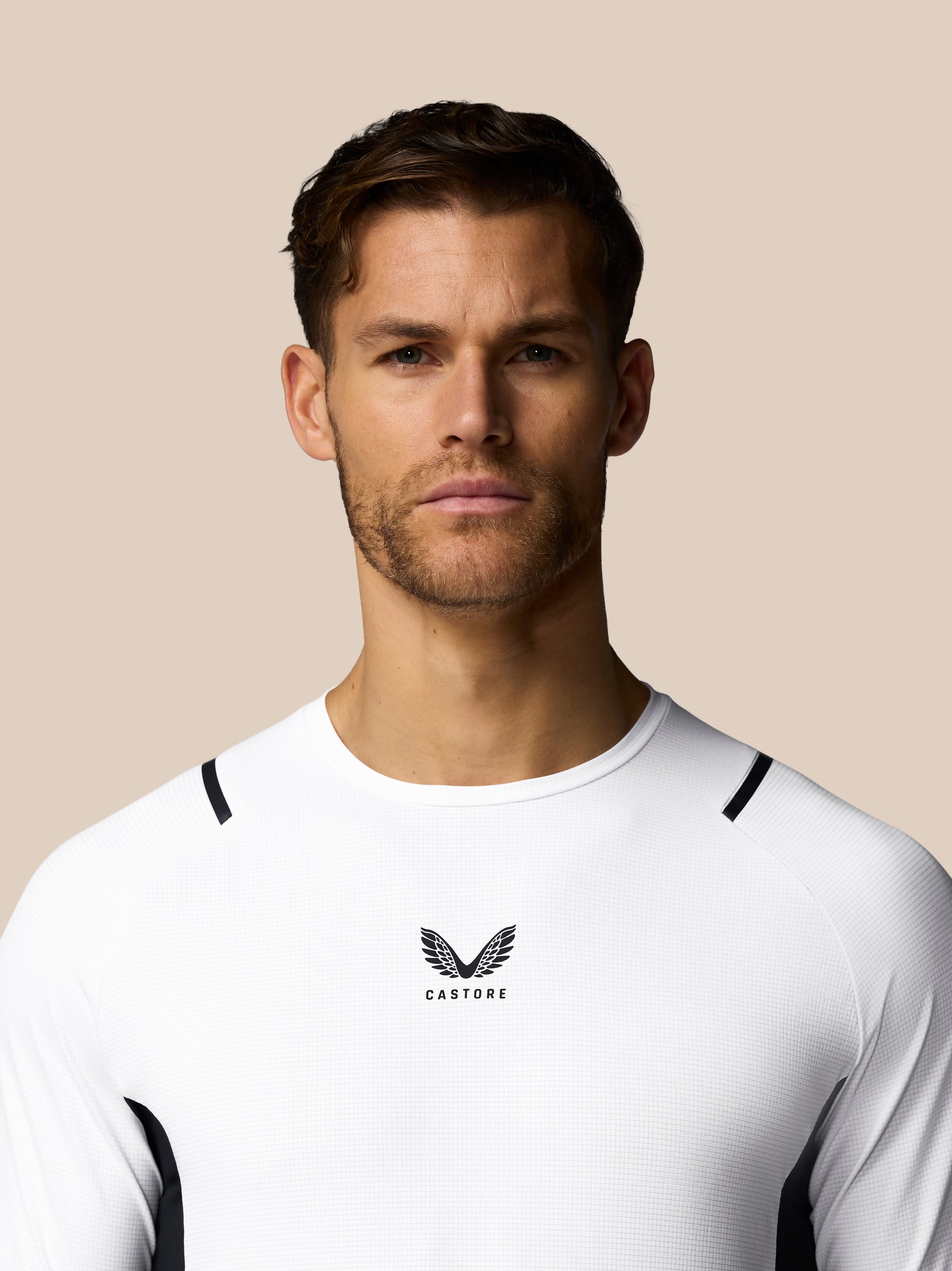 Man wearing a white athletic shirt with a logo on a beige background