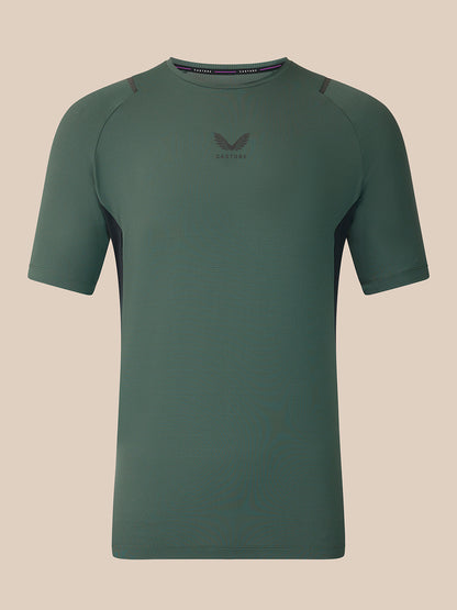 A dark green short-sleeve athletic t-shirt with a subtle winged logo and 'CASTORE' text on the center chest, displayed against a solid beige background.
