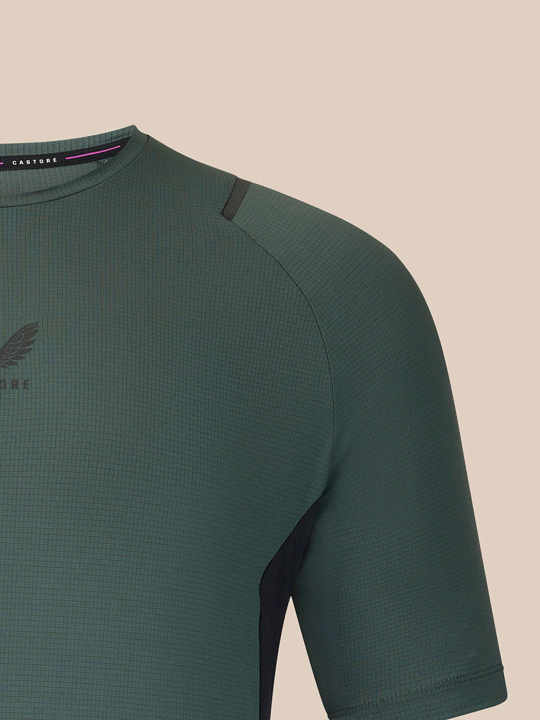 Close-up of a textured short-sleeve athletic top in dark green, showing the chest, shoulder, and collar area against a plain beige background.