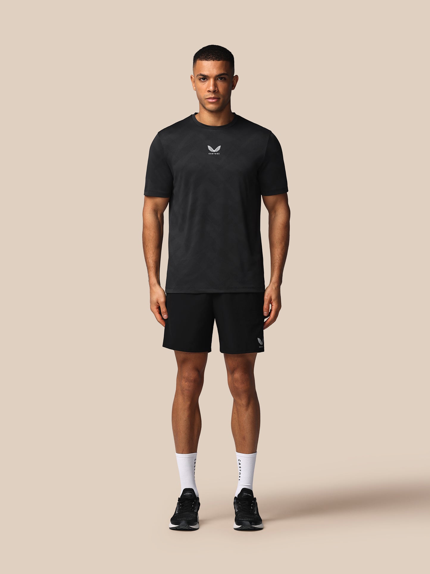 Man wearing a black t-shirt and shorts with a logo on a beige background