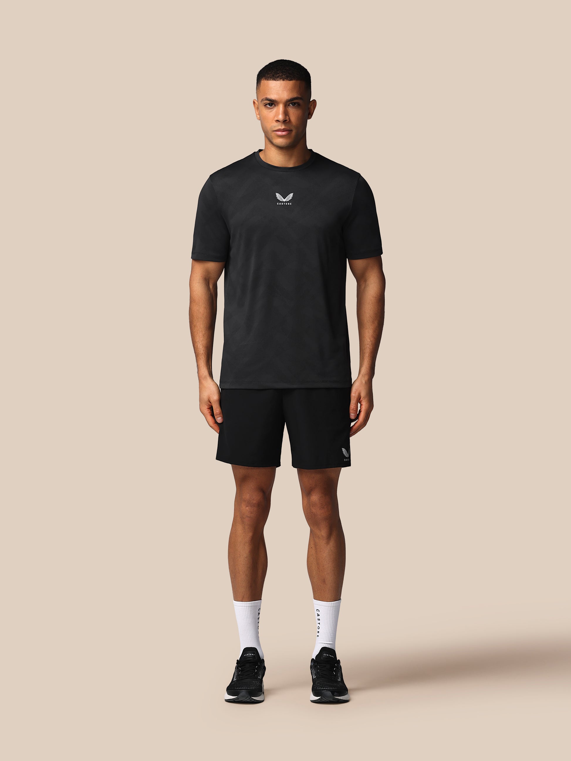 Man wearing a black t-shirt and shorts with a logo on a beige background