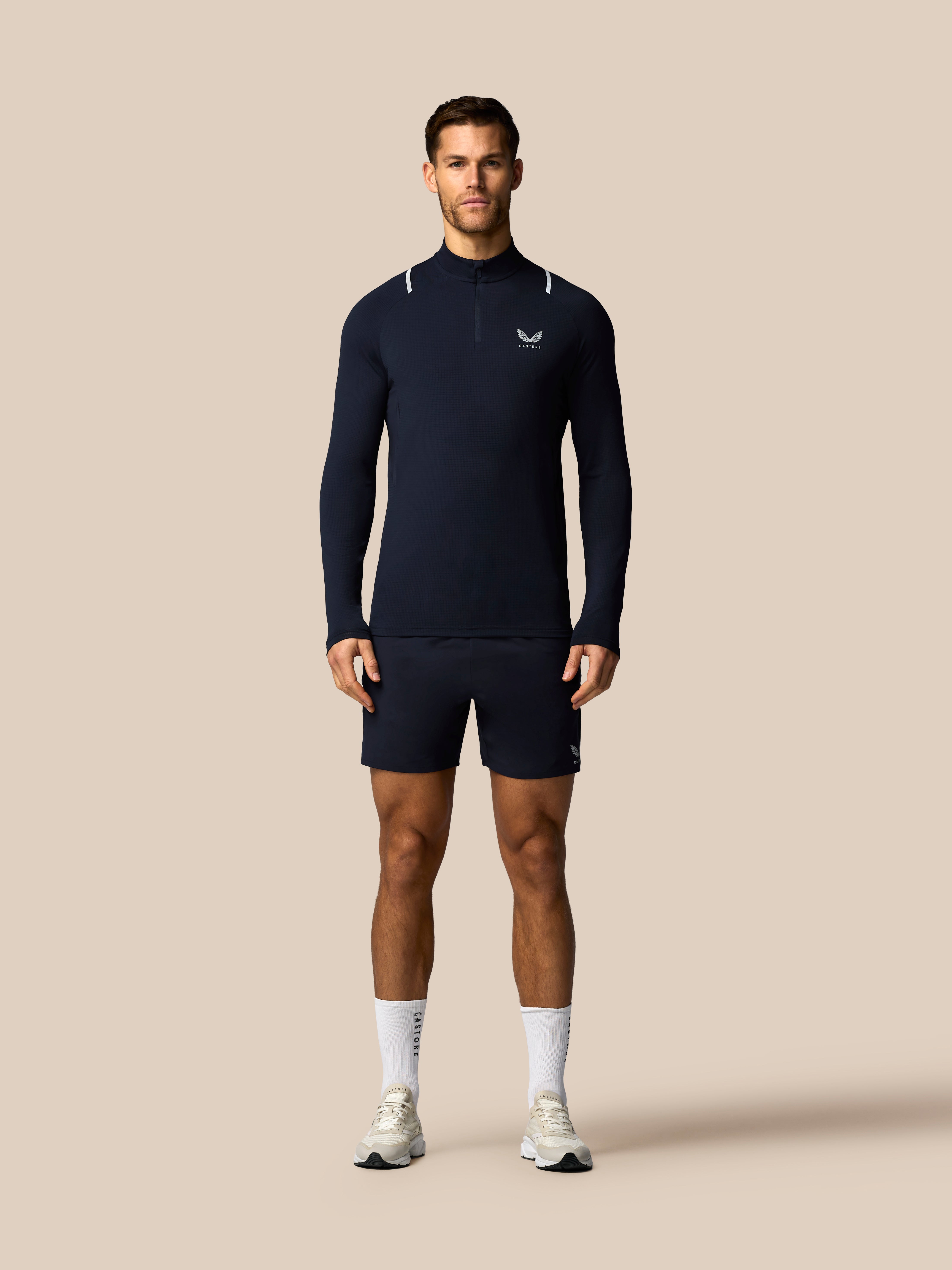 Man wearing a navy long-sleeve athletic shirt and shorts on a beige background