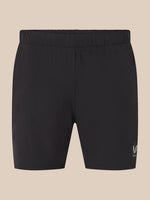 Black athletic shorts with an elastic waistband and a small white embroidered logo on the lower left leg, shown against a solid beige background.
