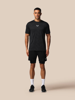 Man wearing a black t-shirt and shorts with a logo on a beige background