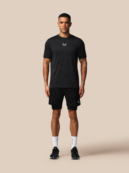 Man wearing a black t-shirt and shorts with a logo on a beige background