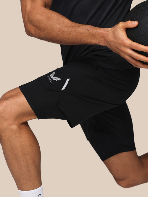 Person wearing black athletic shorts with a logo on a beige background