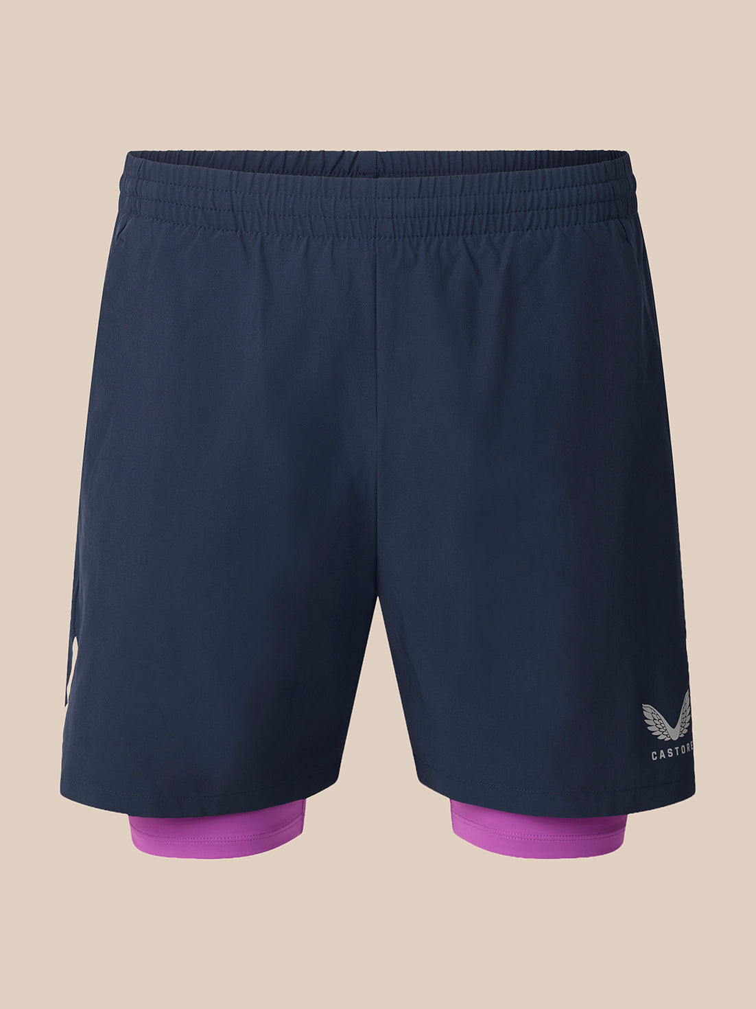 A pair of dark navy blue athletic shorts with a built-in purple inner layer visible at the hem, featuring a white wing logo and the brand name 'CASTORE' on the lower right leg, set against a solid beige background.