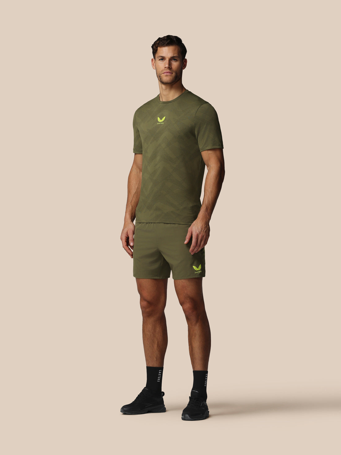 Man wearing an olive green t-shirt and shorts set with a logo on a beige background