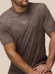 Man wearing a brown athletic t-shirt with a logo on a beige background