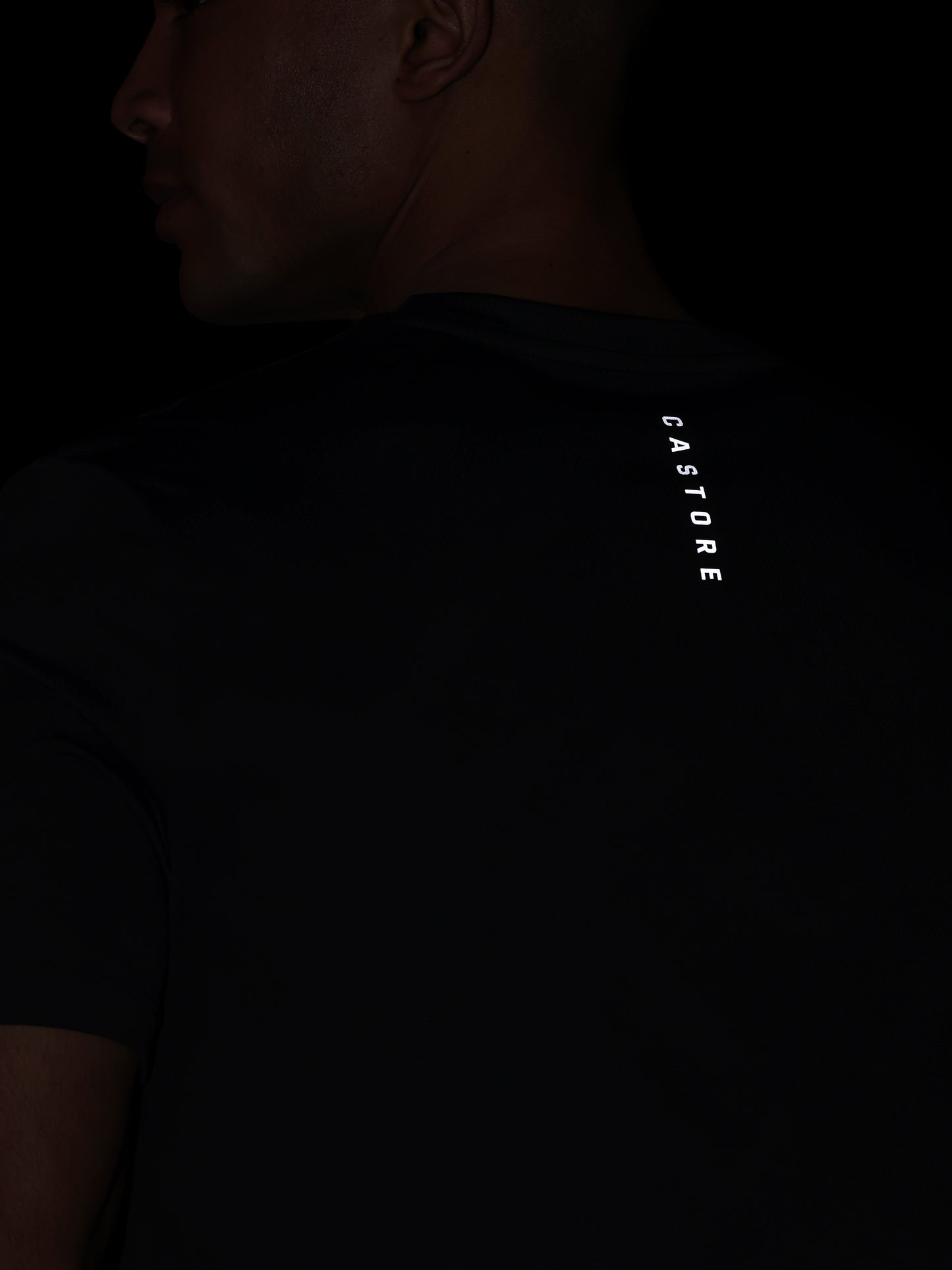 Person wearing a black t-shirt with 'CASTORE' branding on the back against a dark background