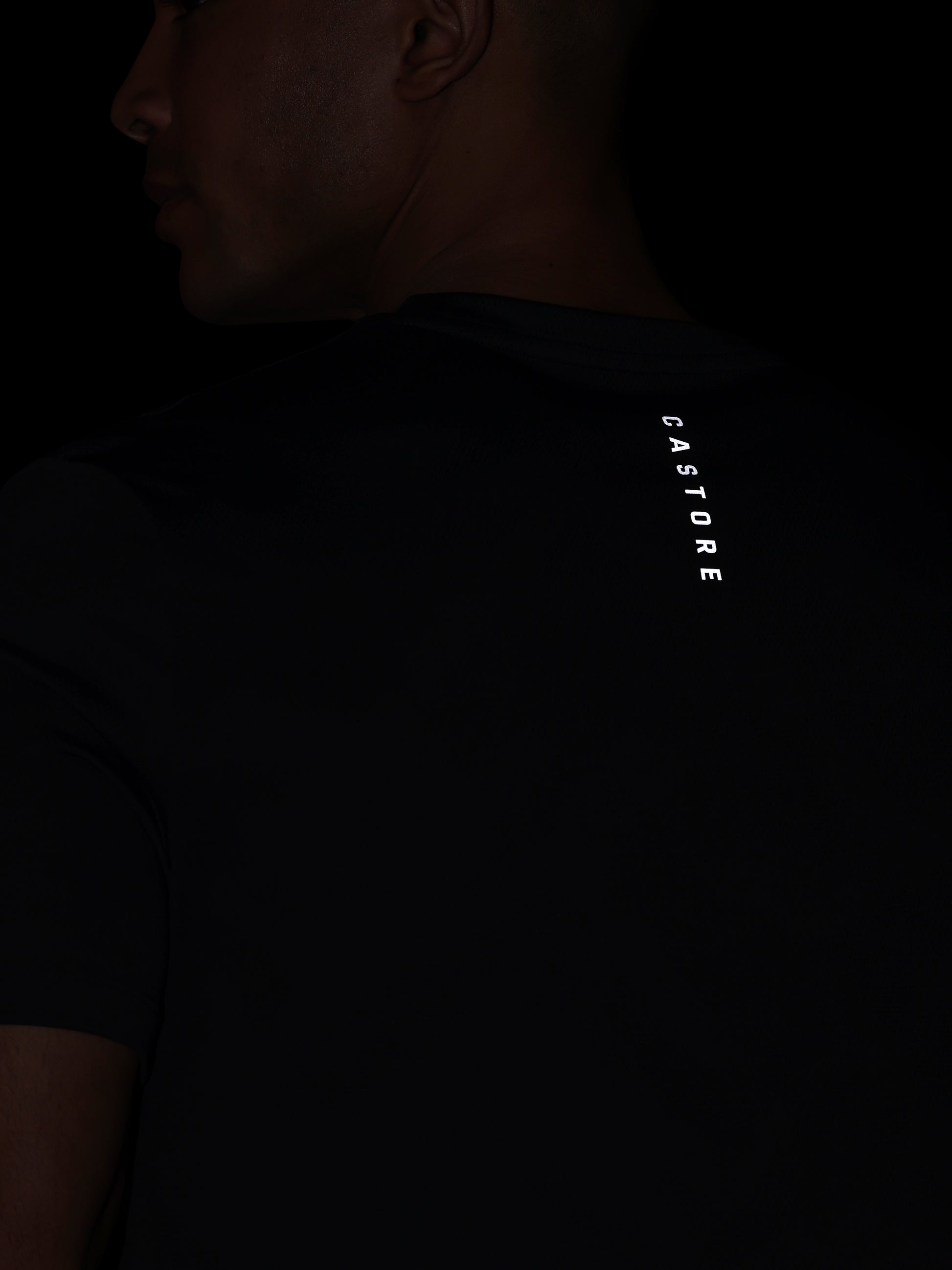 Person wearing a black t-shirt with 'CASTORE' branding on the back against a dark background