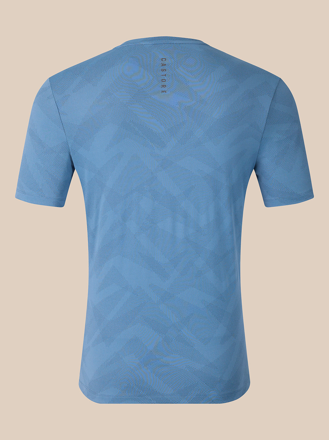 A light blue short-sleeve t-shirt with a subtle geometric pattern, shown from the back against a solid beige background. The brand name 'CASTORE' is printed vertically near the upper back neckline.