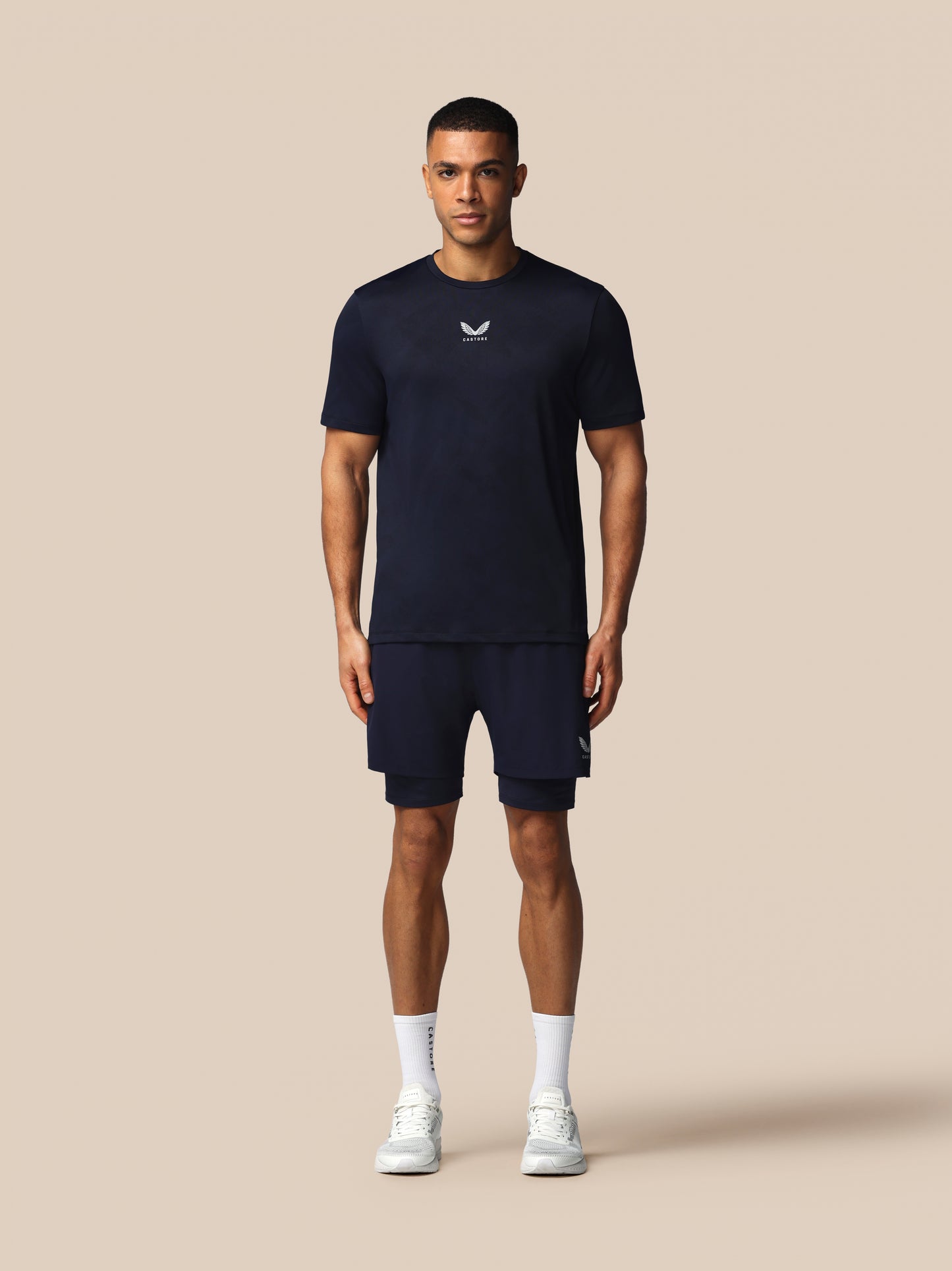 Man wearing a navy blue t-shirt and shorts set with a logo on a beige background