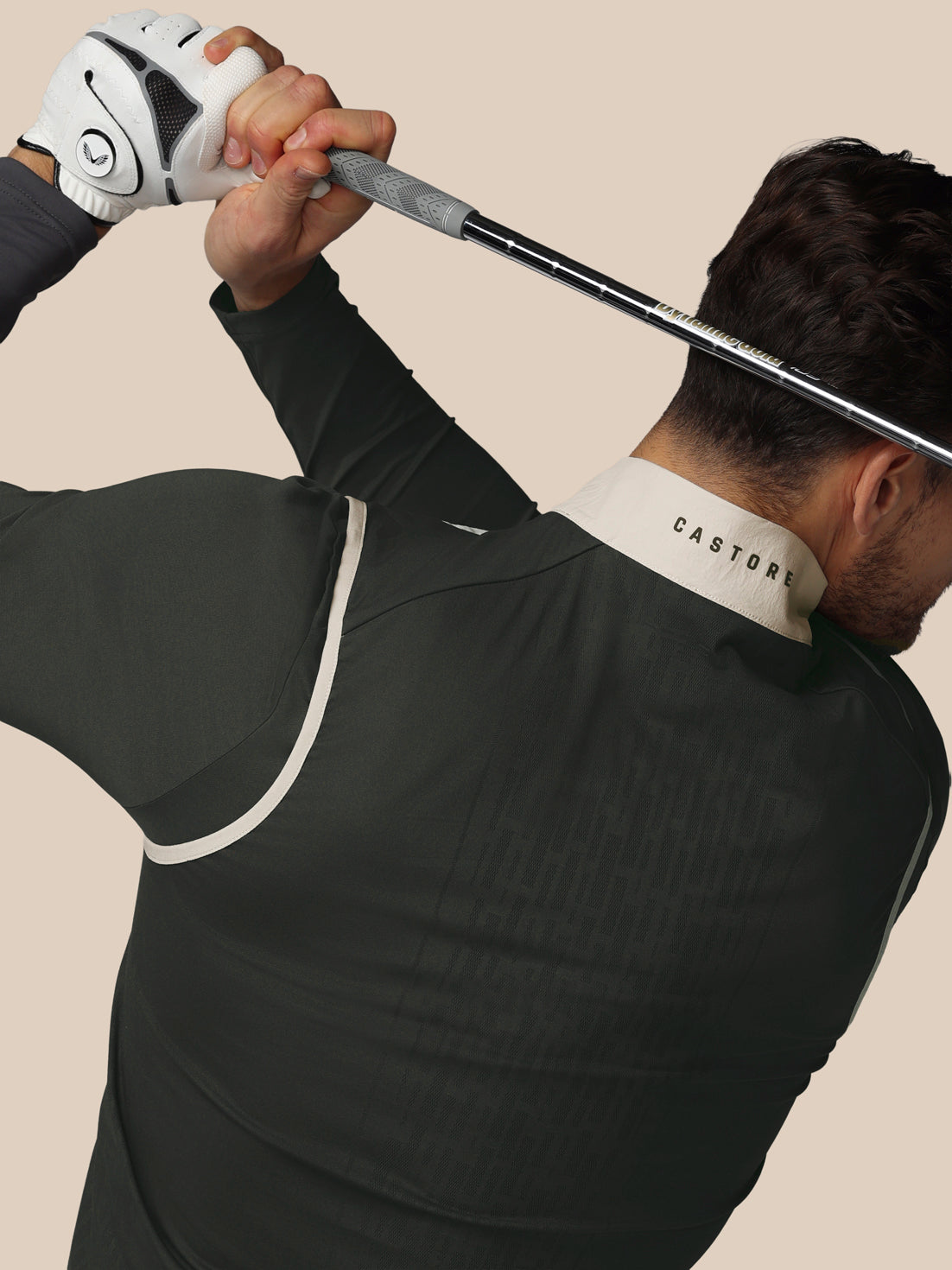 Person in black athletic outfit with 'Castore' branding holding a golf club against a beige background
