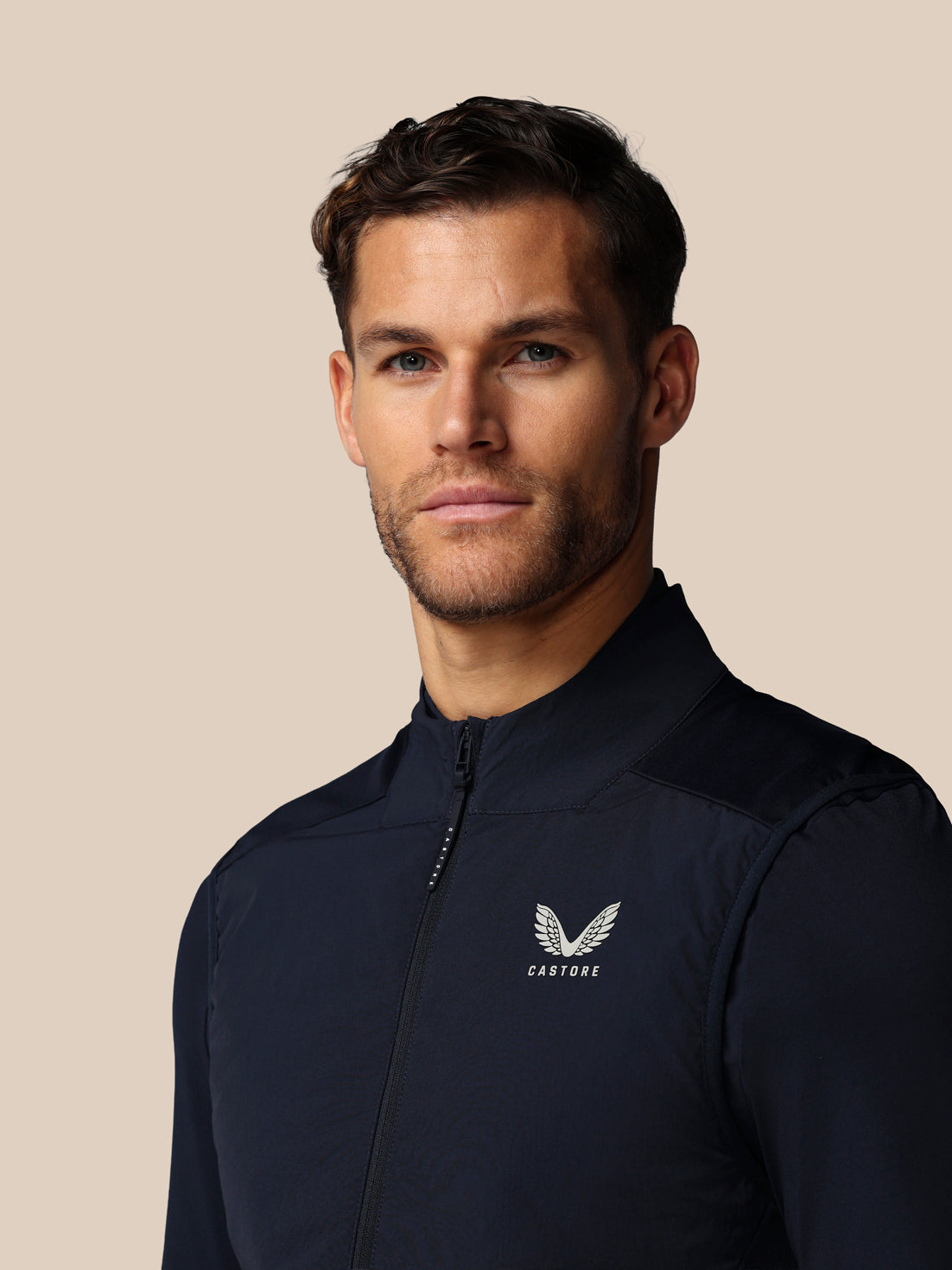 Man wearing a dark blue jacket with a logo on a beige background