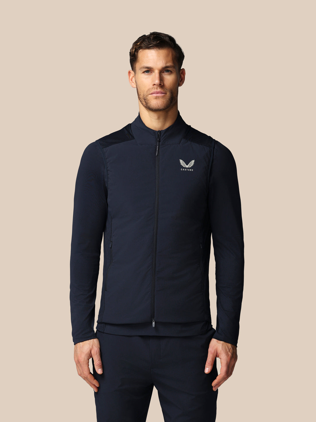 Man wearing a navy jacket with a logo on a beige background