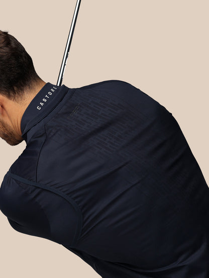 Man wearing a navy blue shirt with 'Castore' branding, holding a golf club.