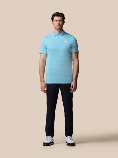 Man wearing a light blue striped polo shirt and dark pants on a beige background