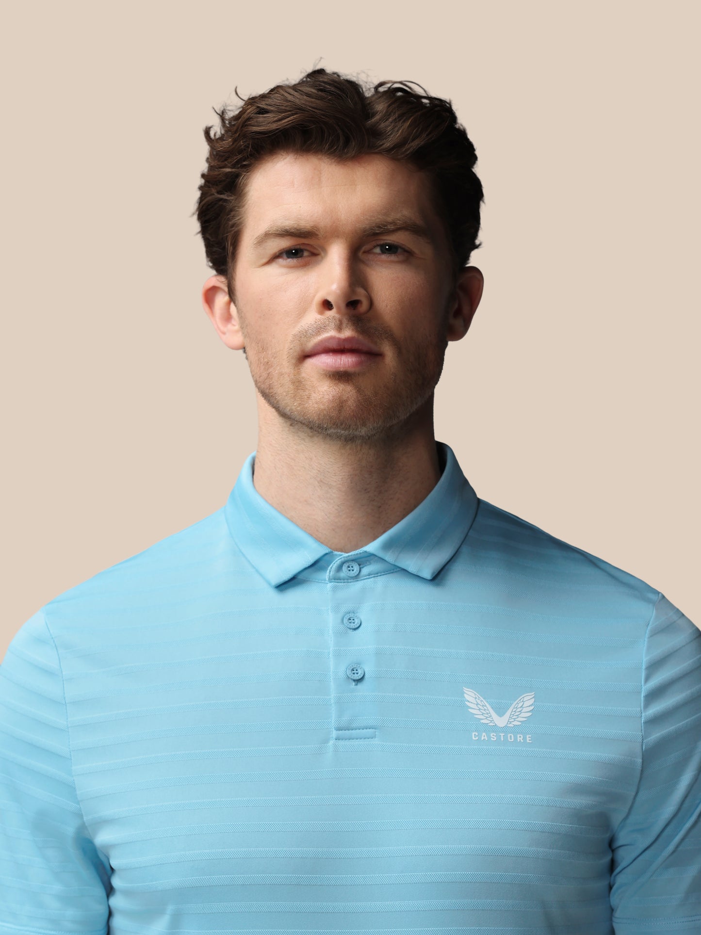 Man wearing a light blue polo shirt with a logo on a beige background